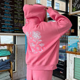 Person wearing a pink hoodie with floral designs in a store setting